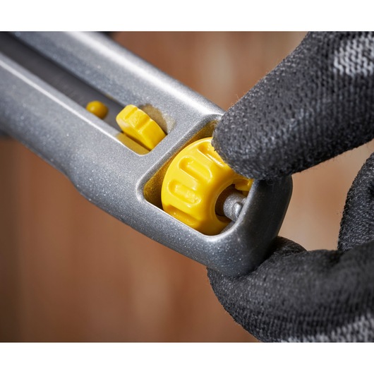 STANLEY 0-10-018 utility knife close-up, showing yellow adjustment wheel being turned with gloved hand.