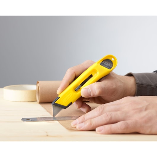 STANLEY 0-10-088 utility knife with yellow handle cutting paper alongside a metal ruler on a wooden table.