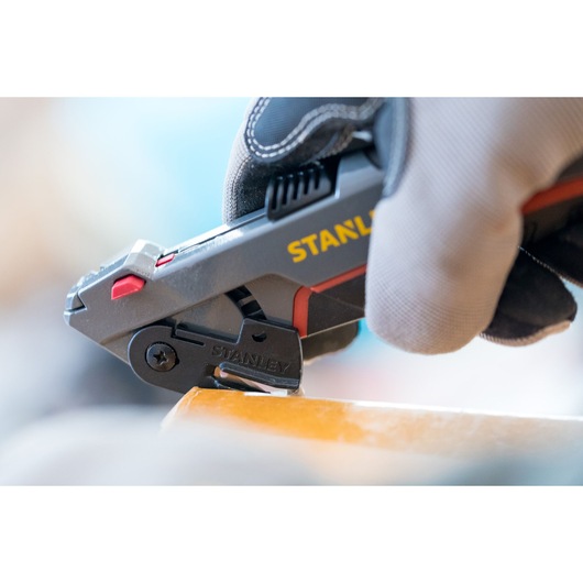 STANLEY 0-10-242 utility knife in use, close-up view, gloved hand holding tool, cutting material.