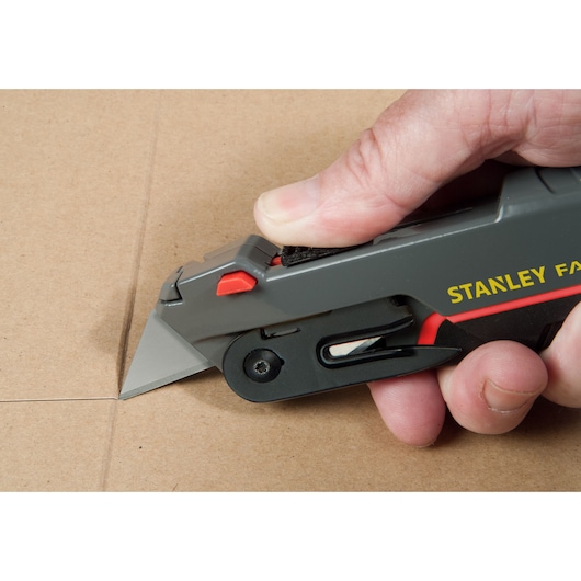 STANLEY 0-10-242 utility knife cutting cardboard, close-up side angle photo.