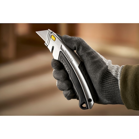 Photo of STANLEY 0-10-788 utility knife held in gloved hand, silver body with black grip and yellow button.