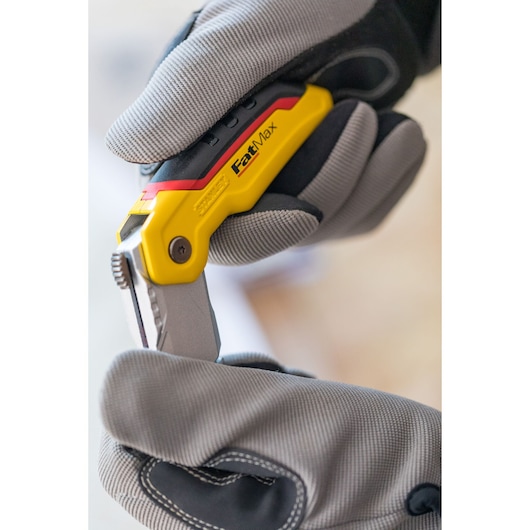 Photo of STANLEY 0-10-825 folding utility knife held in gloved hands, yellow and black handle visible.
