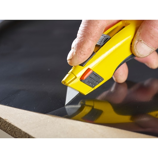 STANLEY 0-11-921 utility knife cutting black sheet, close-up photography of product in use.
