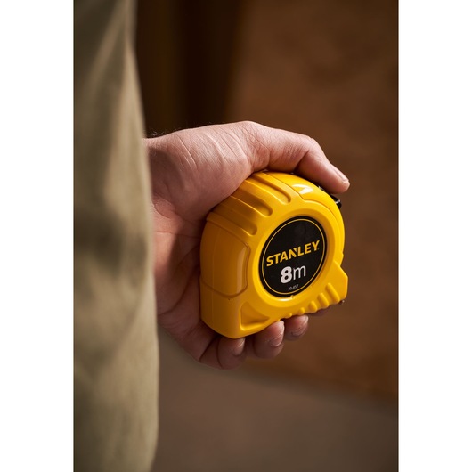 Photo of STANLEY 0-30-457 yellow 8m tape measure held in a hand, product photography.