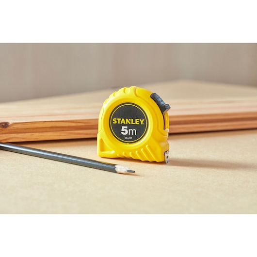 STANLEY 0-30-497 yellow 5m tape measure on a workbench with a pencil and piece of wood in the background.