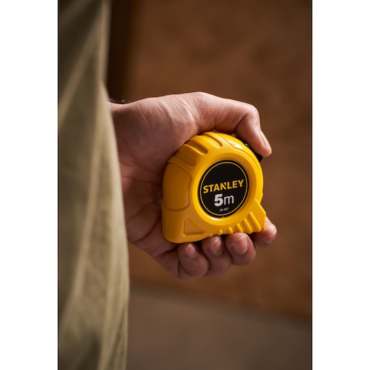 Photo of STANLEY 0-30-497 yellow 5m tape measure held in a hand, product category photography.