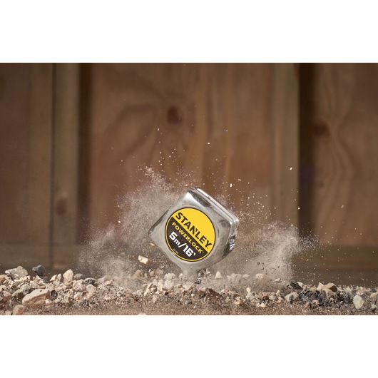 STANLEY 0-33-158 PowerLock tape measure on rocky ground with dust in motion, product photography.