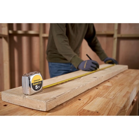 STANLEY 0-33-195 tape measure on wood plank, person marking measurements in workshop setting.