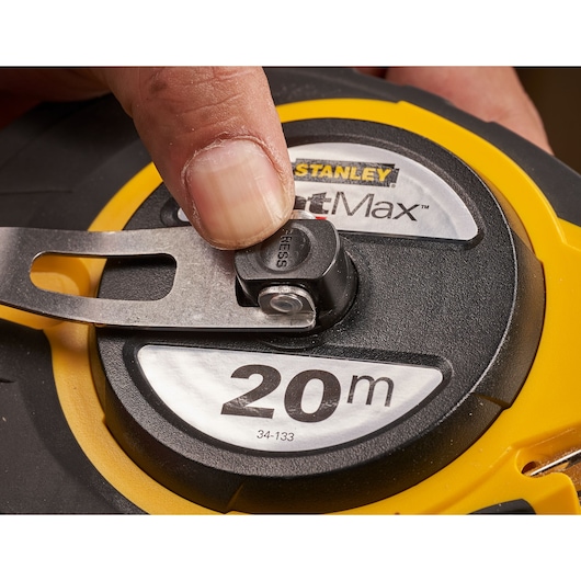 STANLEY 0-34-133 tape measure close-up, yellow and black casing, finger pressing release button.