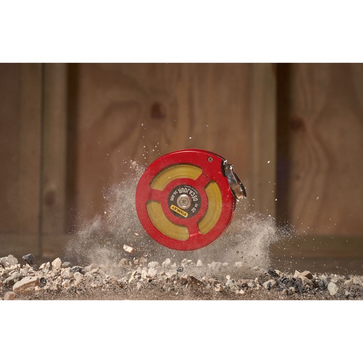 Stanley 0-34-406 red open reel measuring tape on rocky ground, construction setting.