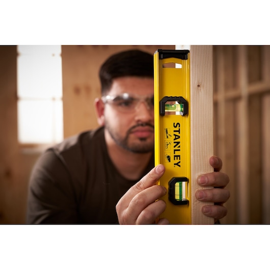 Photo of STANLEY 0-42-072 level tool in use, yellow body, visible vials, held against wooden beam.