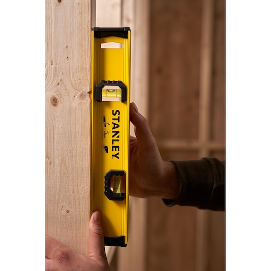 STANLEY 0-42-072 yellow spirit level held vertically against wooden beam, product photography.