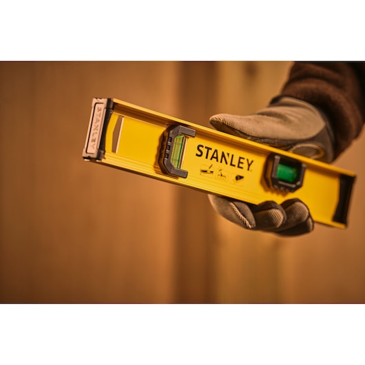 Stanley 0-42-072 spirit level photography, yellow body, held by gloved hand, close-up view.