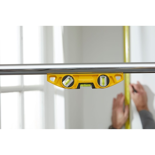 STANLEY 0-43-603 yellow spirit level attached to metal pipe, measuring surface in indoor setting.