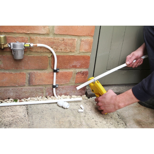 STANLEY 0-70-450 pipe cutter tool cutting white plastic pipe outdoors near brick wall.