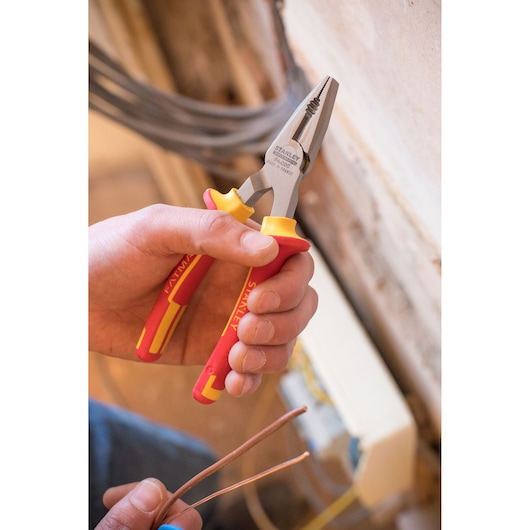 Photo of STANLEY 0-84-000 insulated combination pliers with red and yellow handles being used to cut copper wire.