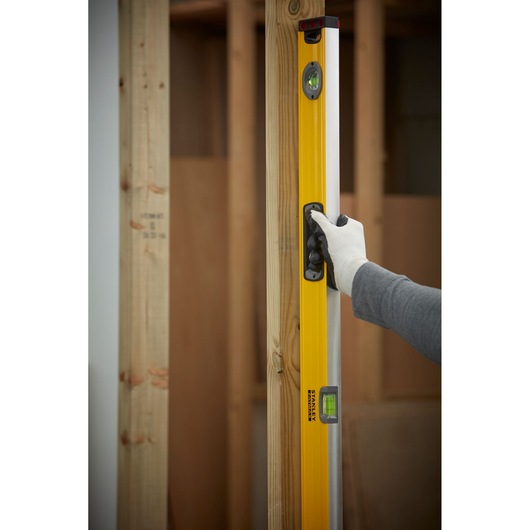 STANLEY 1-43-548 level tool held vertically against wooden frame, user wearing glove.