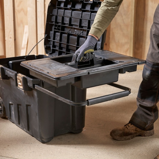 STANLEY 1-92-978 black rolling tool box with removable tray being lifted by a gloved hand in a workshop.