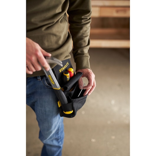 Photo of a person wearing a STANLEY tool belt pouch SKU 1-93-329 holding hand tools, indoor workshop setting.