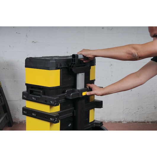 STANLEY 1-95-621 stackable tool box trolley, yellow and black, being handled by a person in a workshop.