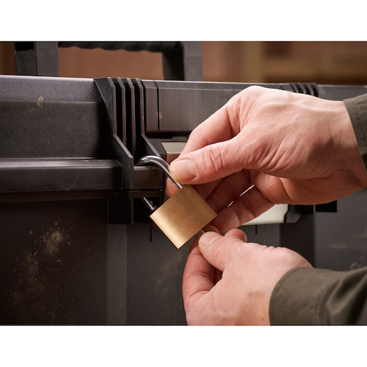 Close-up of hands locking a black toolbox with a brass padlock.
