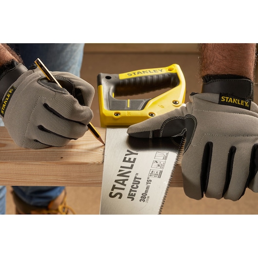 STANLEY 2-15-594 hand saw in use, gloved hands marking wood, pencil and yellow handle visible.