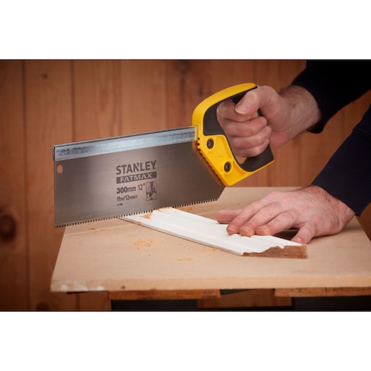 Stanley 2-17-199 hand saw with yellow handle cutting white molding on workbench, side angle.