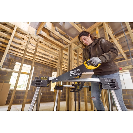STANLEY 2-20-180 hand saw with yellow handle cutting wood on sawhorse at construction site.