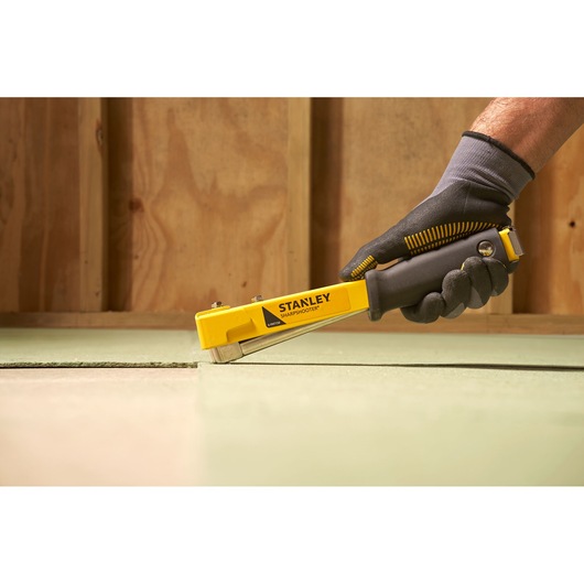 Photo of STANLEY 6-PHT150 staple gun being used on flooring, black and yellow design, side angle.