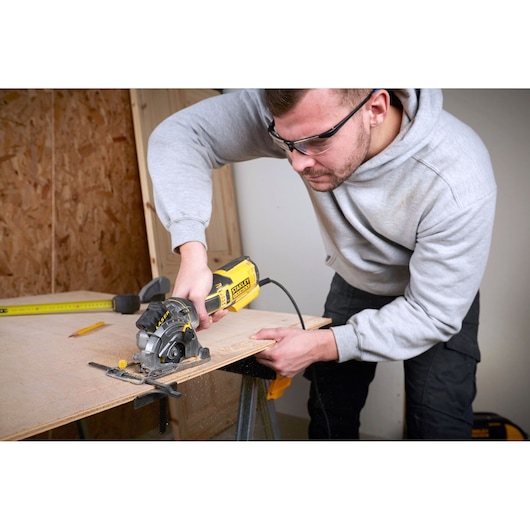 STANLEY FME380K circular saw in use cutting plywood, close-up of tool held by person in workshop.
