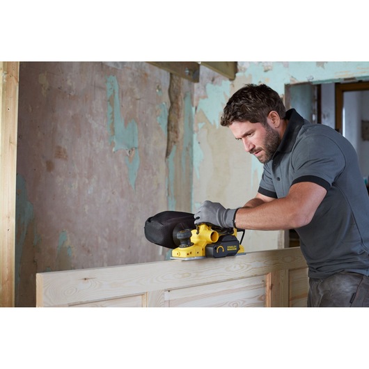 Photo of STANLEY FME630 belt sander in use on wood surface during renovation, side view.