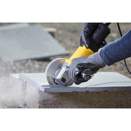 Photo of STANLEY FMEG220KA angle grinder cutting a tile, worker wearing gloves outdoors.
