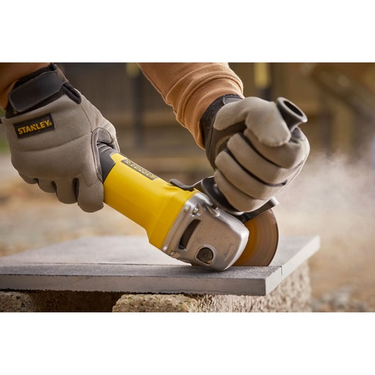 Photo of STANLEY FMEG225VS grinder cutting stone slab outdoors, worker wearing protective gloves.