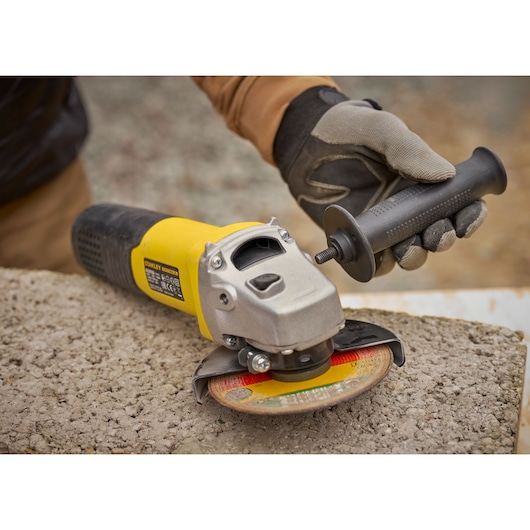 STANLEY FMEG225VS angle grinder with yellow body, side handle being attached, outdoor setting.