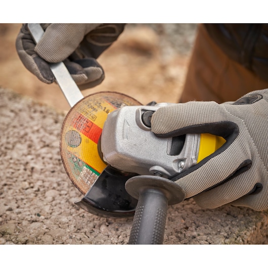 STANLEY FMEG225VS angle grinder in use, close-up, showing gloved hands and grinding wheel on rough surface.