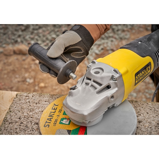 STANLEY FMEG232 angle grinder closeup with handle being attached outdoors on concrete surface.