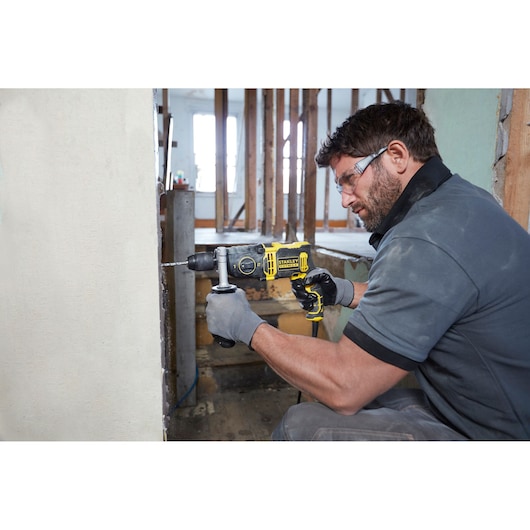 STANLEY FMEH850K hammer drill in use, drilling into a wall, construction site setting.