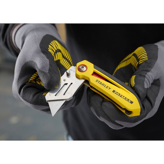 STANLEY FMHT0-10827 yellow folding utility knife held in gloved hands, close-up.