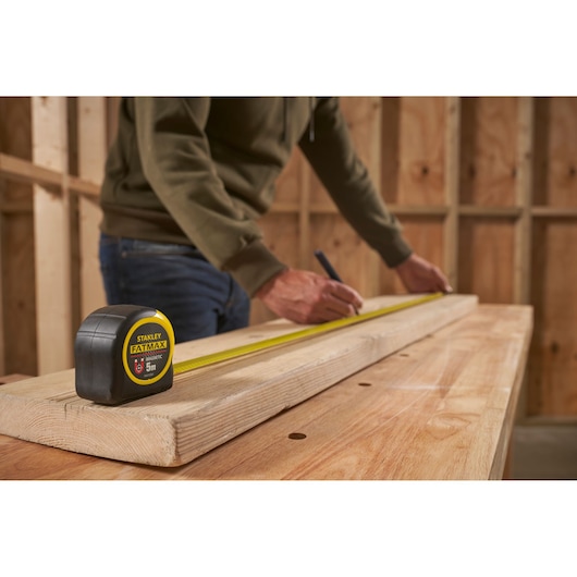 STANLEY FMHT0-33864 tape measure on wood in workshop setting, person marking measurement.