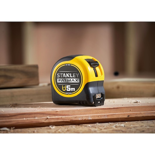 Stanley FMHT0-33864 FatMax magnetic tape measure, 5m, black and yellow, side angle, on wood.