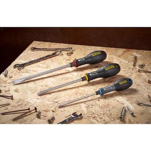 Photo of three STANLEY FMHT0-62624 screwdrivers with colored rings on a wooden workbench, surrounded by screws.