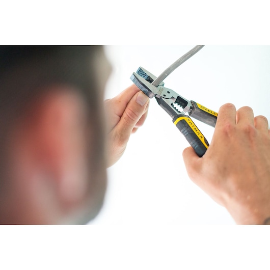 Stanley FMHT0-75469 pliers with yellow and black grips held by hands cutting a cable in close-up.