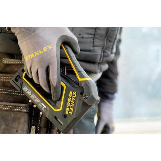 STANLEY FMHT0-80550 stapler held by gloved hand, close-up angle, with tool pouch in background.