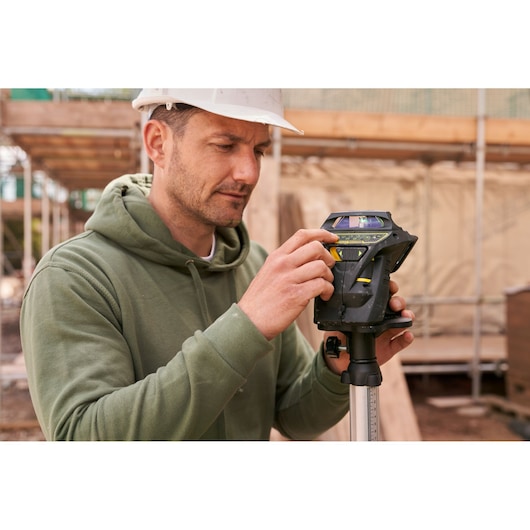 Photo of STANLEY FMHT1-77356 rotary laser level on tripod being adjusted by worker at construction site.