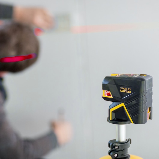STANLEY FMHT1-77414 laser level on tripod, projecting red line on wall, close-up photography.