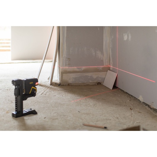 STANLEY FMHT1-77415 laser level projecting red lines on walls in construction setting, side angle.