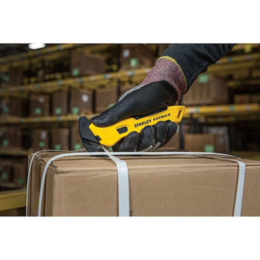 Stanley FMHT10358-0 utility knife held by gloved hand cutting box strap in warehouse.