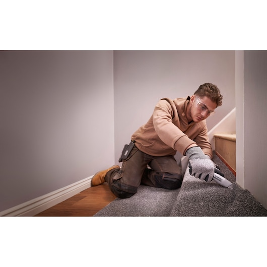 Photo of a worker using a STANLEY FMHT10501-0 utility knife to cut carpet on stairs.