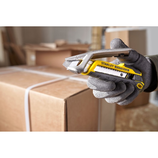 Photo of STANLEY FMHT10594-0 FATMAX utility knife held in gloved hand, angled over cardboard box.