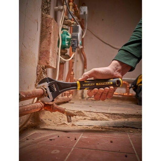 STANLEY FMHT13126-0 adjustable wrench being used on copper pipes in a construction setting.